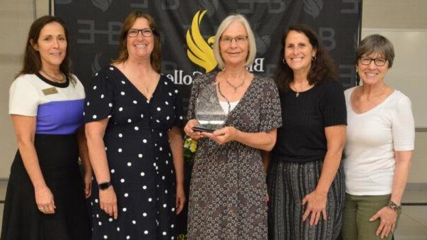 5 people standing in front of backdrop with 1 holding an award